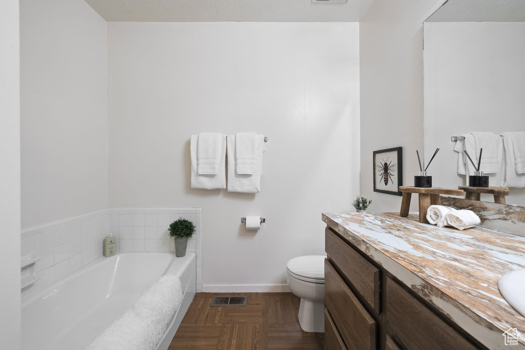 Bathroom with vanity with extensive cabinet space, toilet, a bathing tub, and parquet flooring