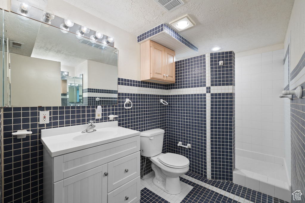 Bathroom with vanity with extensive cabinet space, tile walls, tile flooring, tasteful backsplash, and toilet