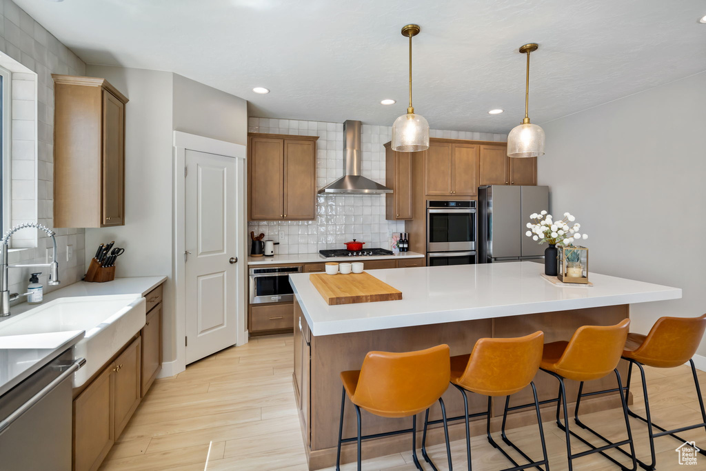 Kitchen featuring appliances with stainless steel finishes, a kitchen island, hanging light fixtures, tasteful backsplash, and wall chimney exhaust hood