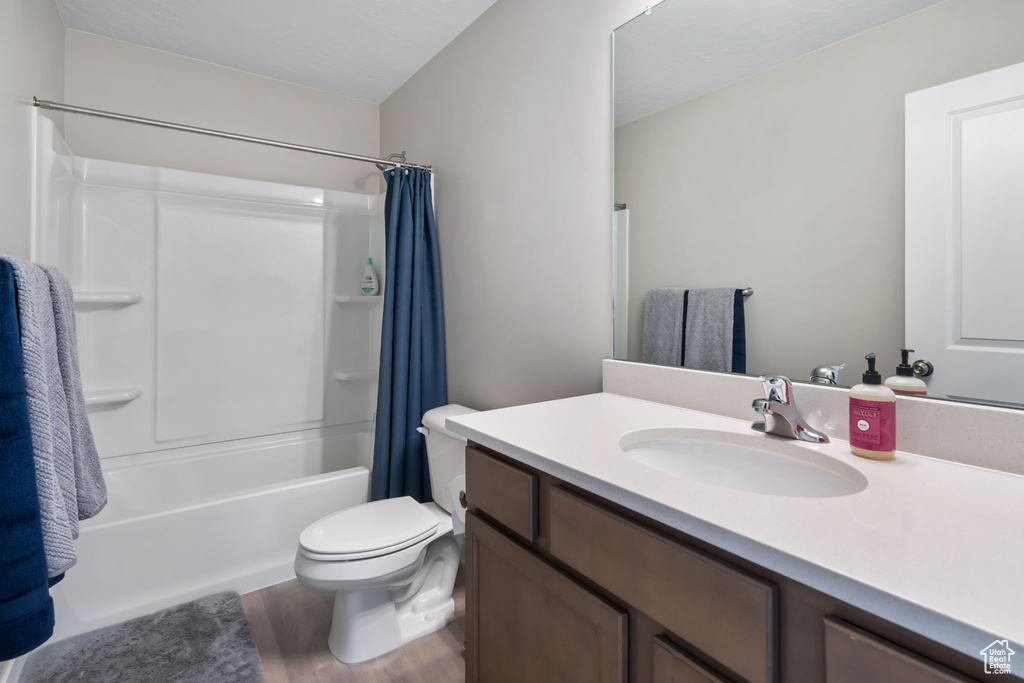 Full bathroom with vanity with extensive cabinet space, shower / bath combo, toilet, and hardwood / wood-style flooring