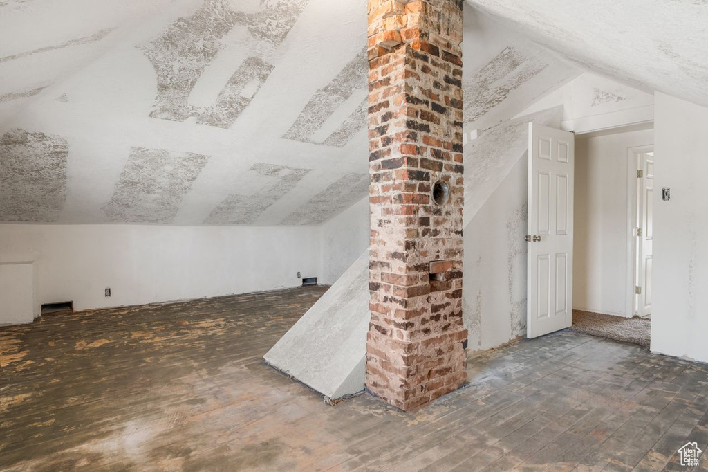 Bonus room featuring lofted ceiling, dark hardwood / wood-style flooring, and brick wall