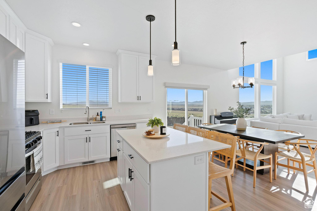 Kitchen with stainless steel appliances, white cabinetry, sink, pendant lighting, and light wood-type flooring