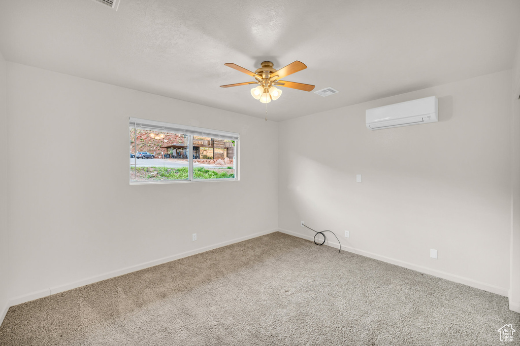 Spare room featuring a wall mounted air conditioner, carpet floors, and ceiling fan