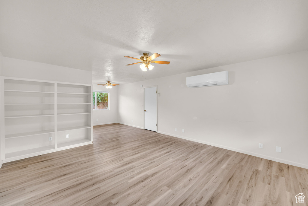 Empty room featuring a wall unit AC, ceiling fan, light hardwood / wood-style floors, and built in shelves