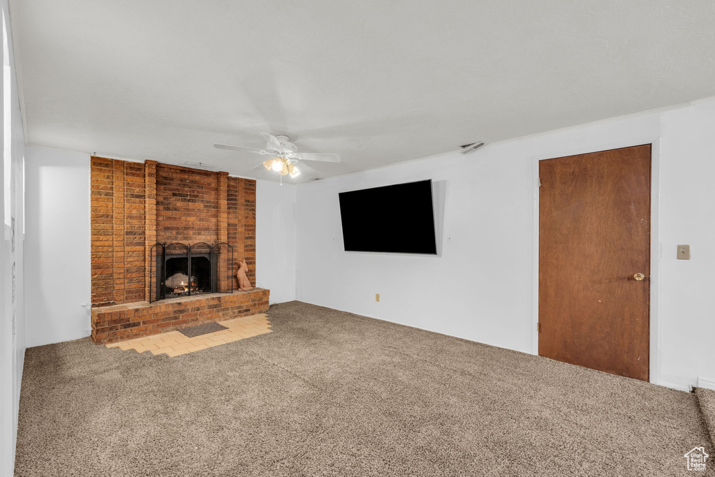 Unfurnished living room with brick wall, ceiling fan, carpet, and a fireplace