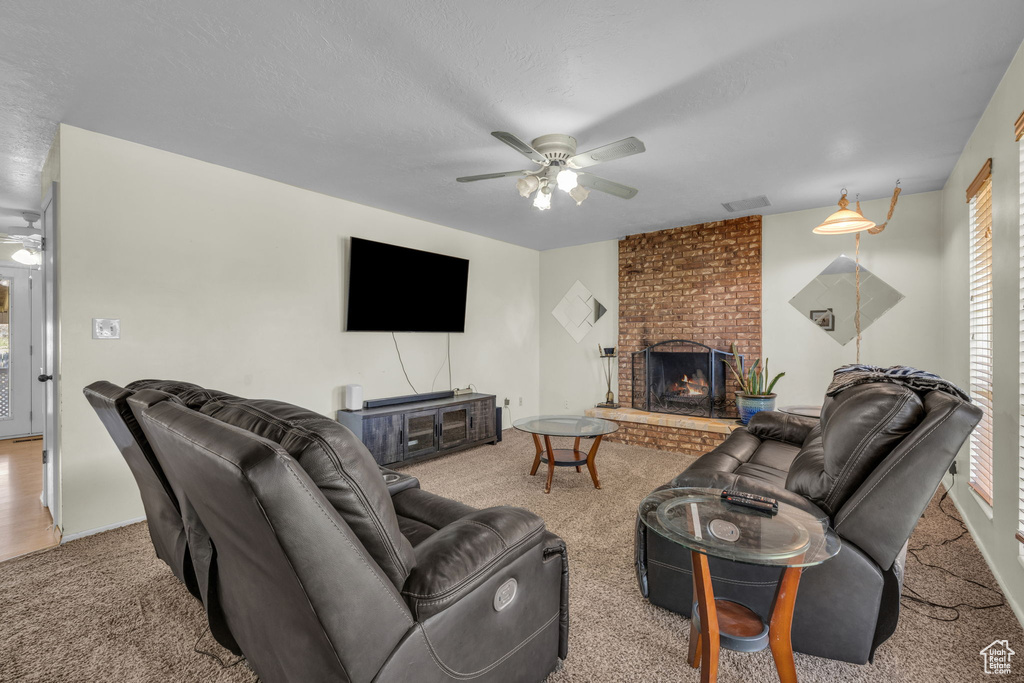 Carpeted living room featuring brick wall, ceiling fan, and a fireplace