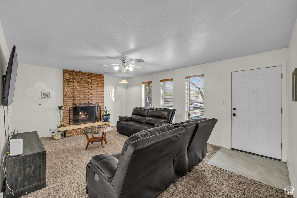 Living room featuring brick wall, ceiling fan, a fireplace, and carpet floors