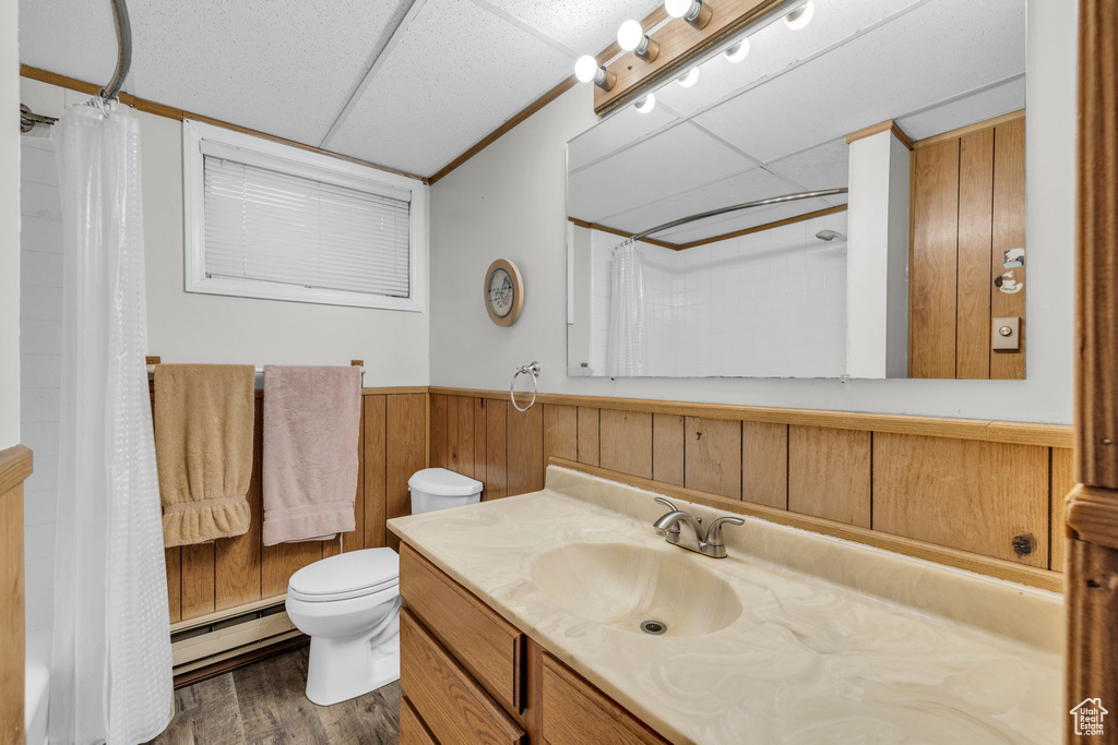 Bathroom with a drop ceiling, toilet, vanity, baseboard heating, and hardwood / wood-style floors