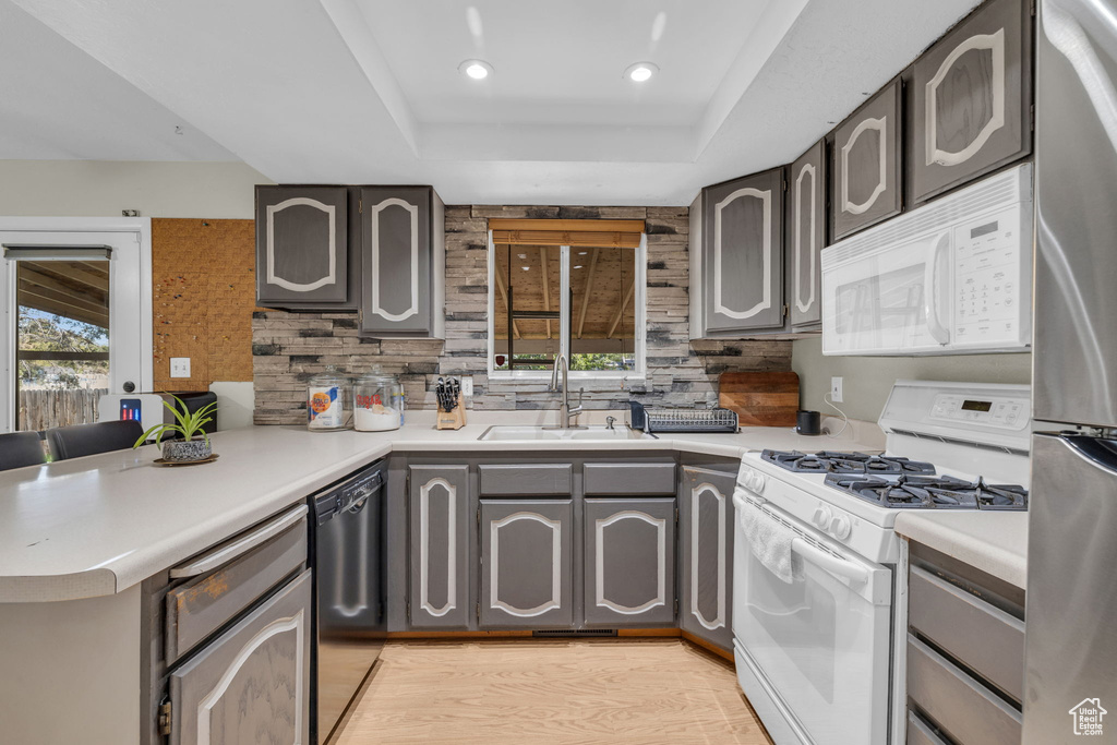Kitchen featuring sink, white appliances, backsplash, and light wood-type flooring