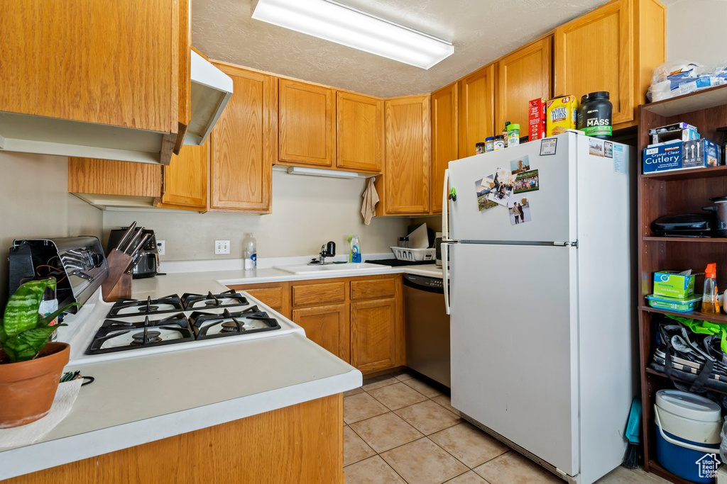 Kitchen featuring range, light tile flooring, white fridge, sink, and stainless steel dishwasher