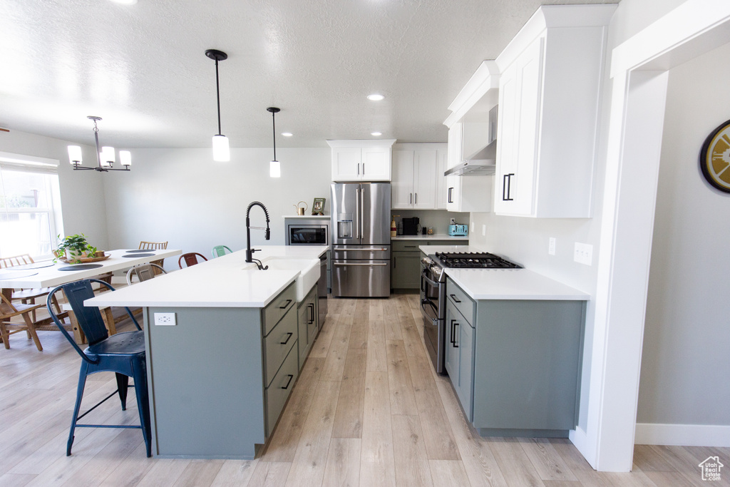 Kitchen with appliances with stainless steel finishes, light hardwood / wood-style floors, a kitchen island with sink, and hanging light fixtures