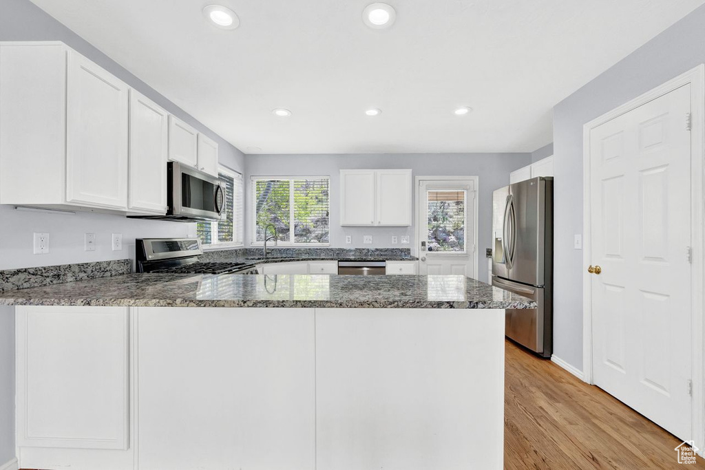 Kitchen featuring appliances with stainless steel finishes, light hardwood / wood-style flooring, kitchen peninsula, and white cabinetry