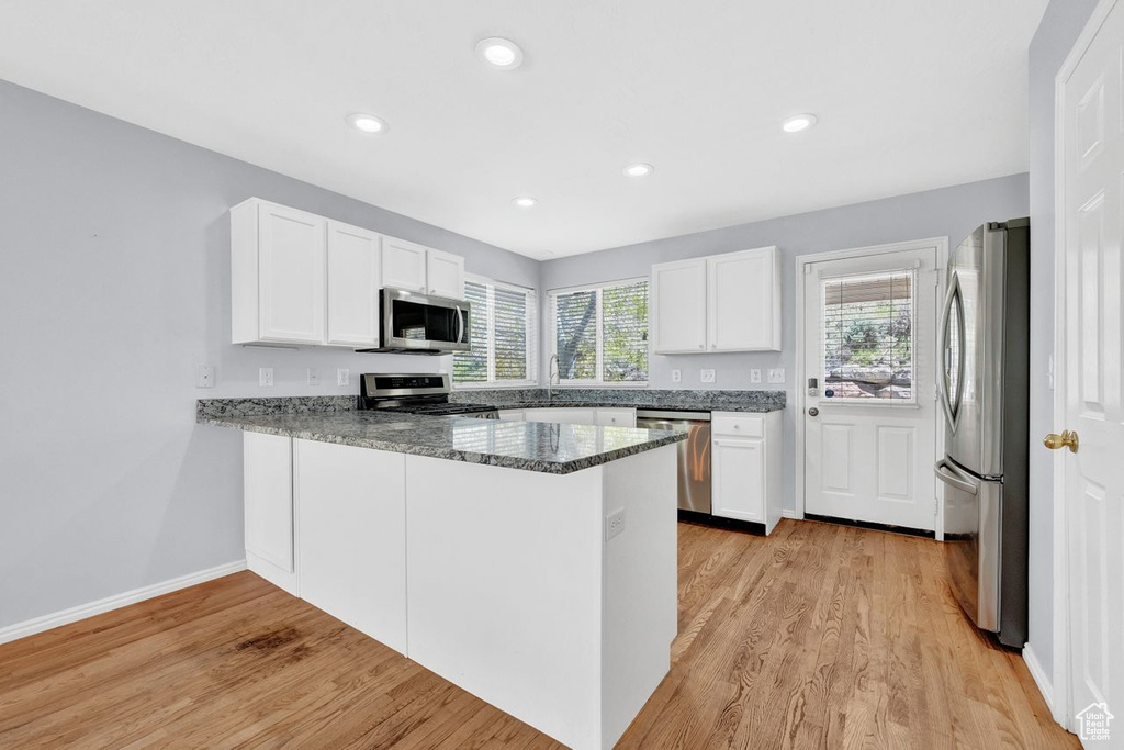 Kitchen featuring stone countertops, white cabinets, light wood-type flooring, stainless steel appliances, and kitchen peninsula
