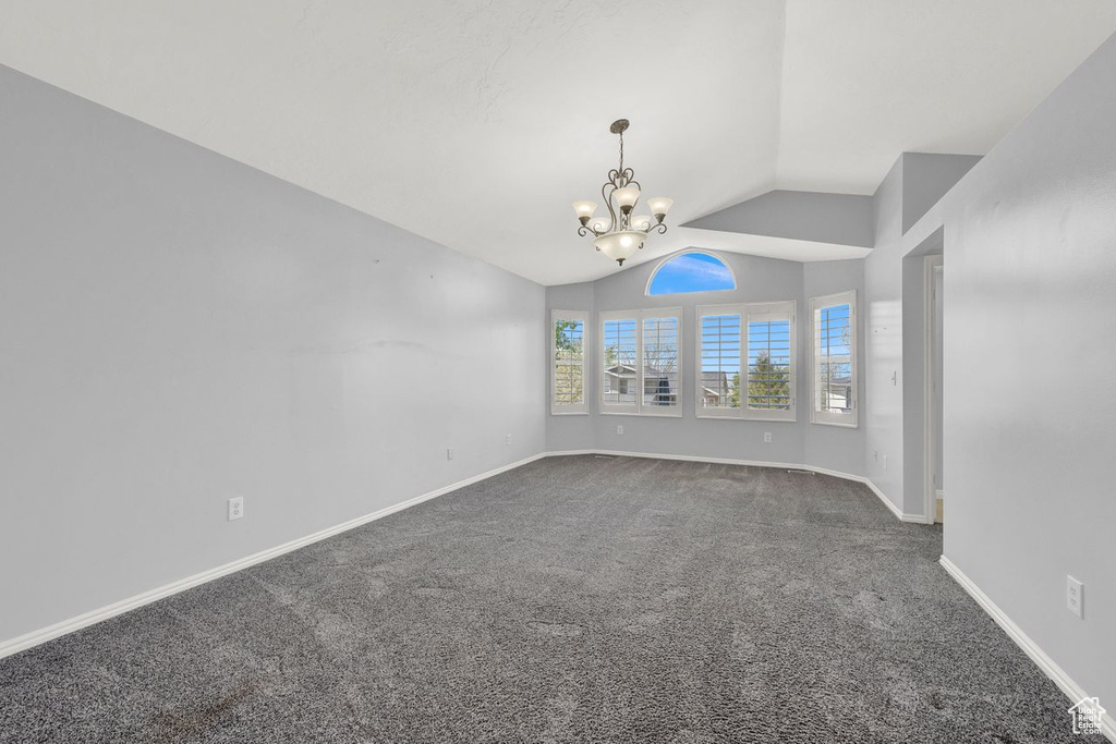 Unfurnished room featuring dark colored carpet, a notable chandelier, and vaulted ceiling