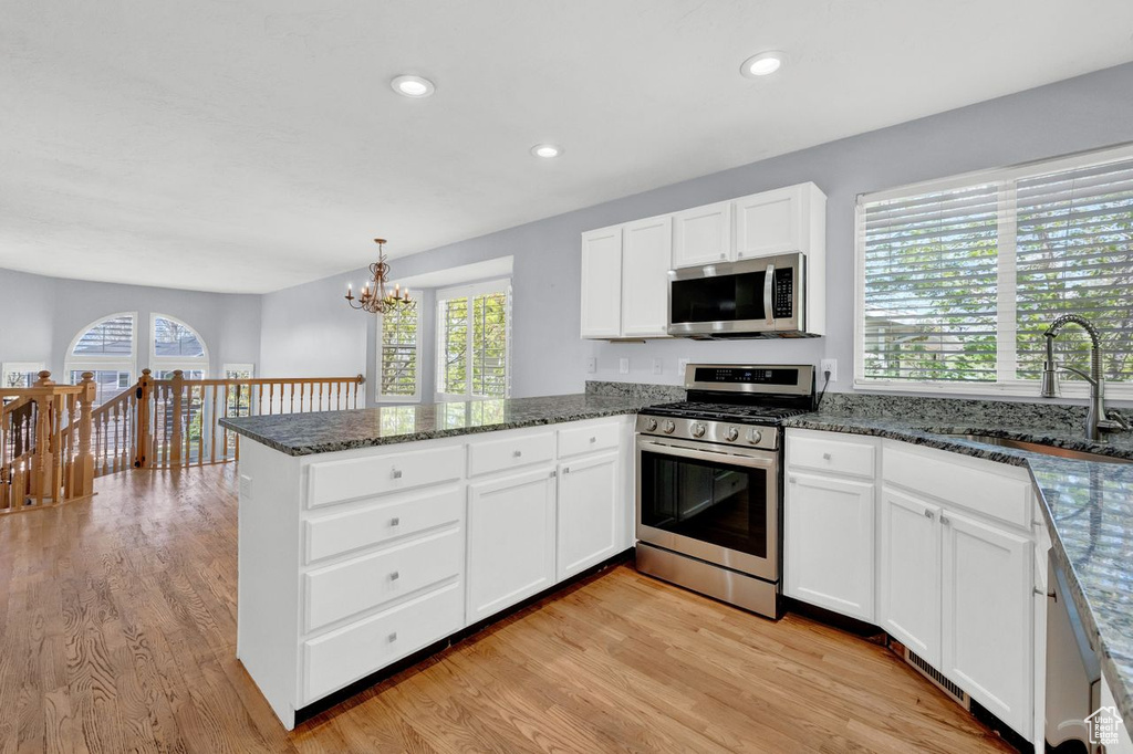 Kitchen with white cabinets, light hardwood / wood-style flooring, kitchen peninsula, appliances with stainless steel finishes, and sink