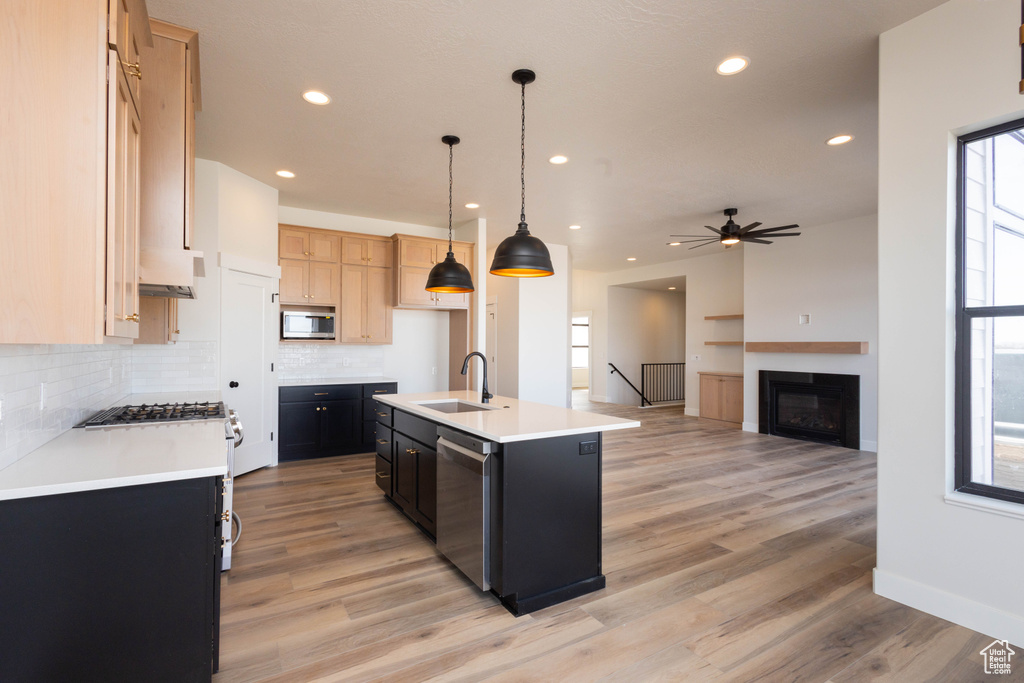 Kitchen featuring sink, backsplash, light wood-type flooring, stainless steel appliances, and an island with sink