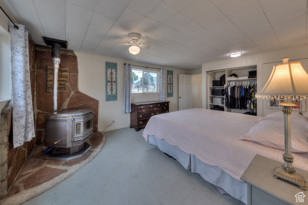 Bedroom with a wood stove, carpet flooring, ceiling fan, and a closet