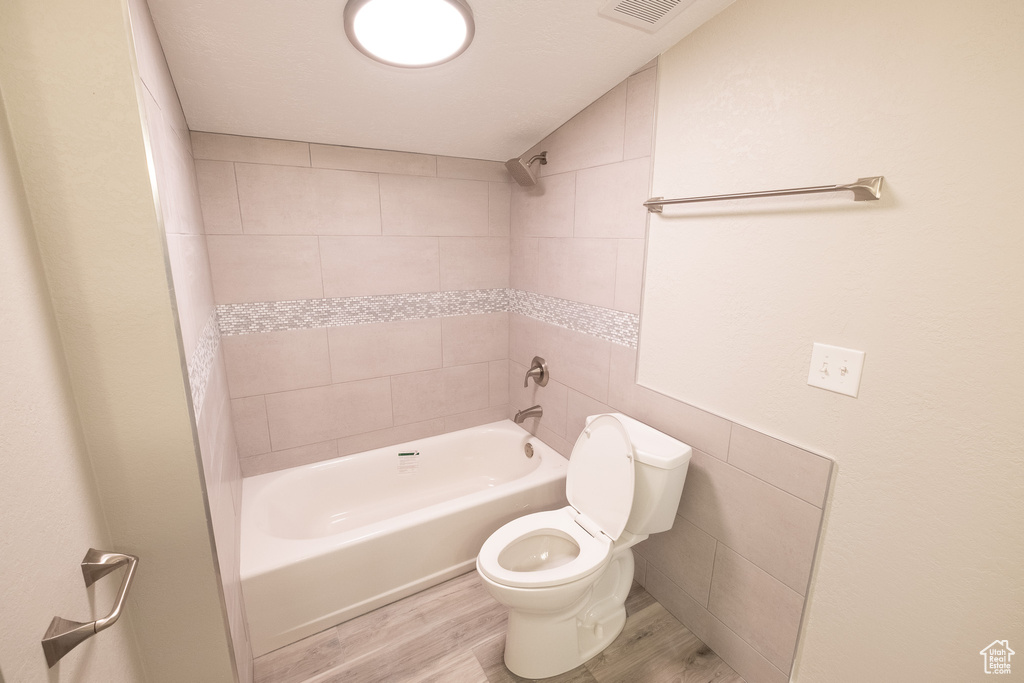 Bathroom featuring tiled shower / bath, toilet, tile walls, and hardwood / wood-style floors