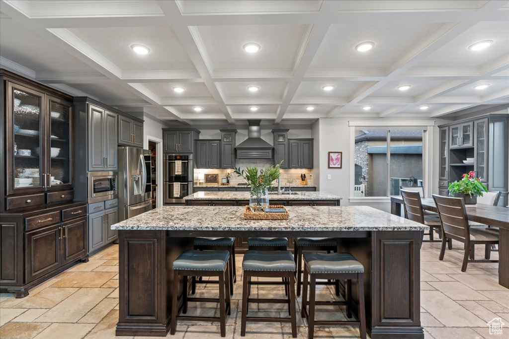 Kitchen with a center island, coffered ceiling, wall chimney range hood, and stainless steel appliances