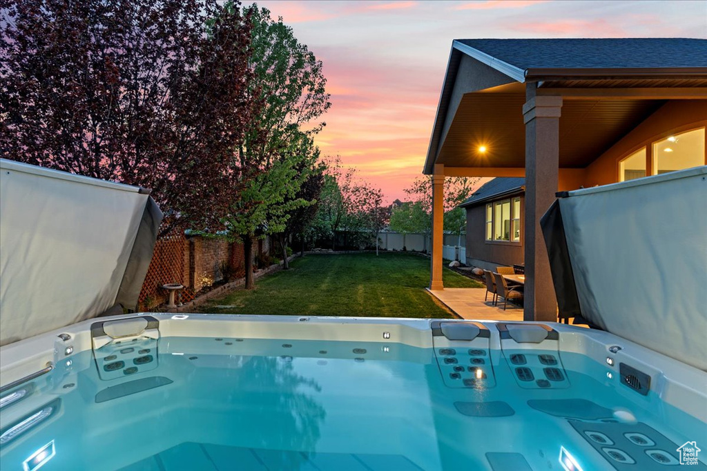 Pool at dusk with a hot tub and a lawn