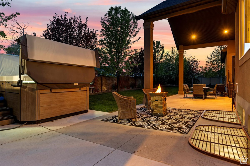 Patio terrace at dusk with a hot tub, an outdoor fire pit, and a lawn