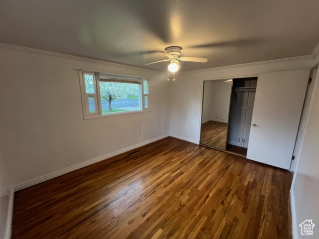 Unfurnished bedroom with a closet, ceiling fan, crown molding, and dark wood-type flooring