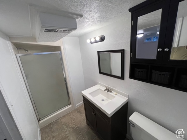 Bathroom with tile flooring, a textured ceiling, toilet, a shower with shower door, and vanity