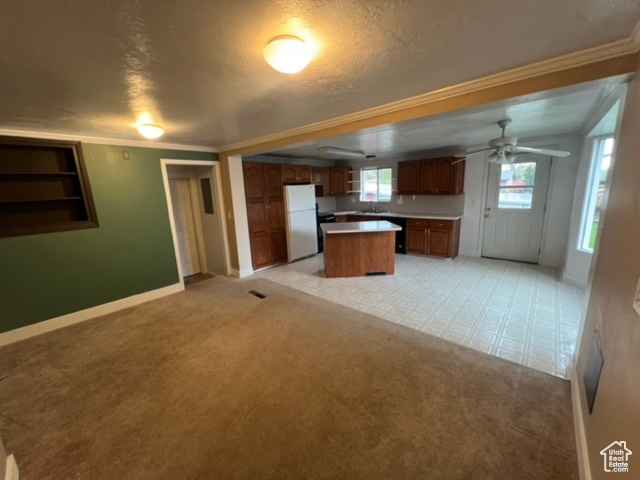 Kitchen with white fridge, a kitchen island, ceiling fan, and light carpet