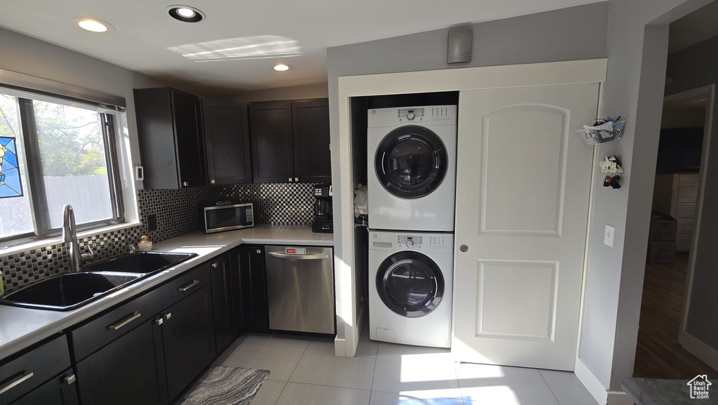 Laundry area featuring stacked washer / dryer, sink, and light tile floors
