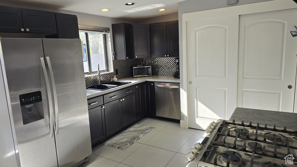Kitchen with backsplash, sink, stainless steel appliances, and light tile floors