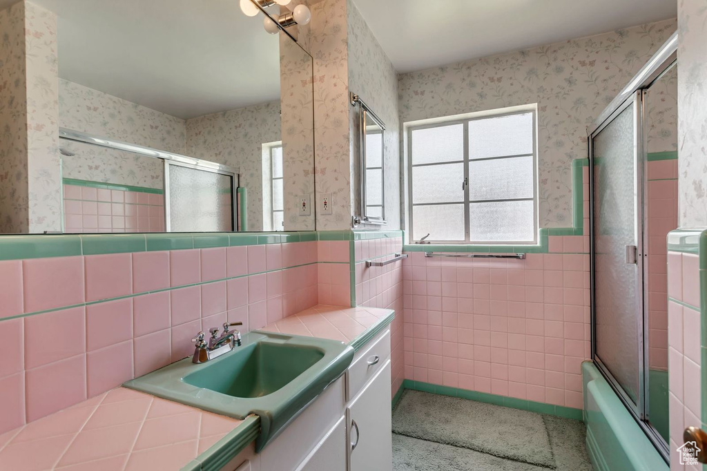 Bathroom featuring tile walls, vanity, backsplash, and bath / shower combo with glass door