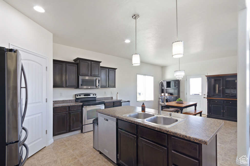 Kitchen featuring hanging light fixtures, stainless steel appliances, a kitchen island with sink, sink, and light tile floors