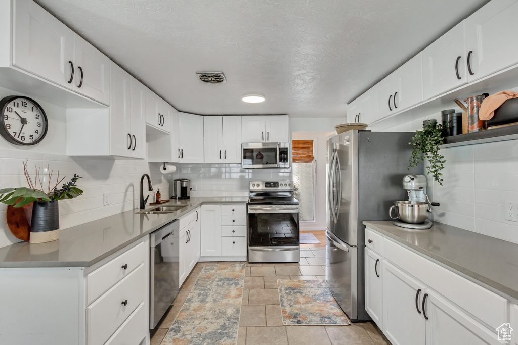 Kitchen featuring light tile flooring, white cabinetry, backsplash, appliances with stainless steel finishes, and sink