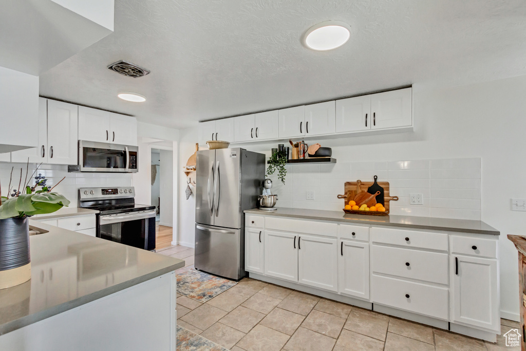 Kitchen featuring appliances with stainless steel finishes, tasteful backsplash, white cabinetry, and light tile floors