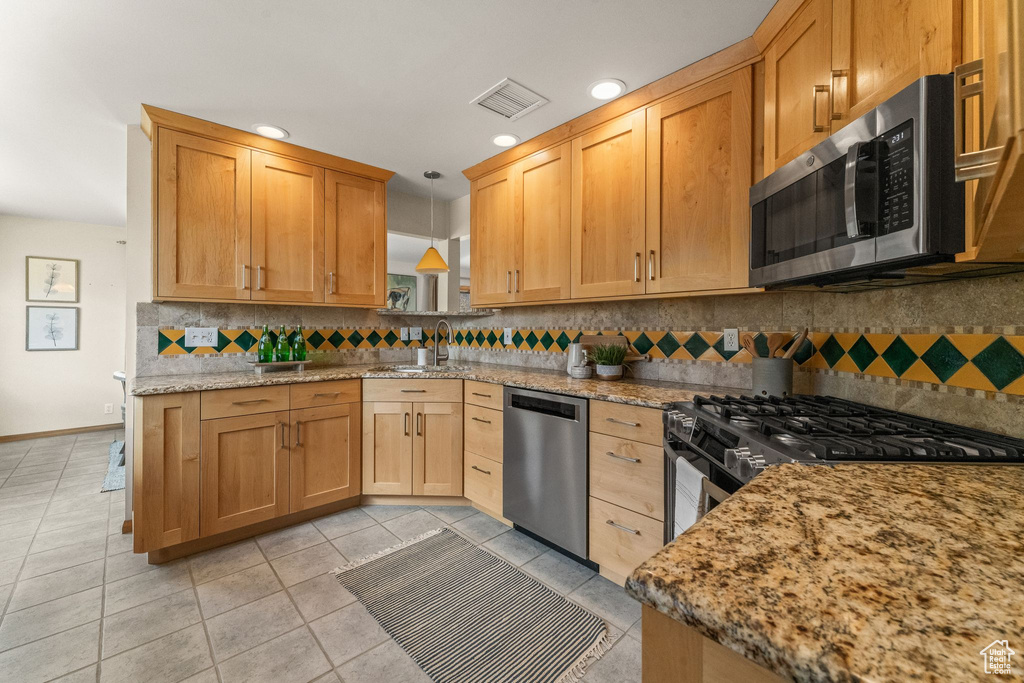 Kitchen featuring pendant lighting, backsplash, appliances with stainless steel finishes, sink, and light tile floors