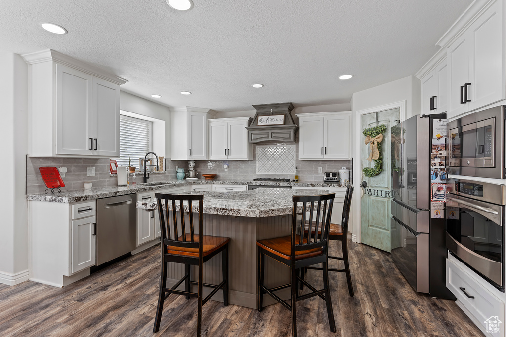 Kitchen featuring a kitchen island, appliances with stainless steel finishes, custom range hood, and dark hardwood / wood-style floors