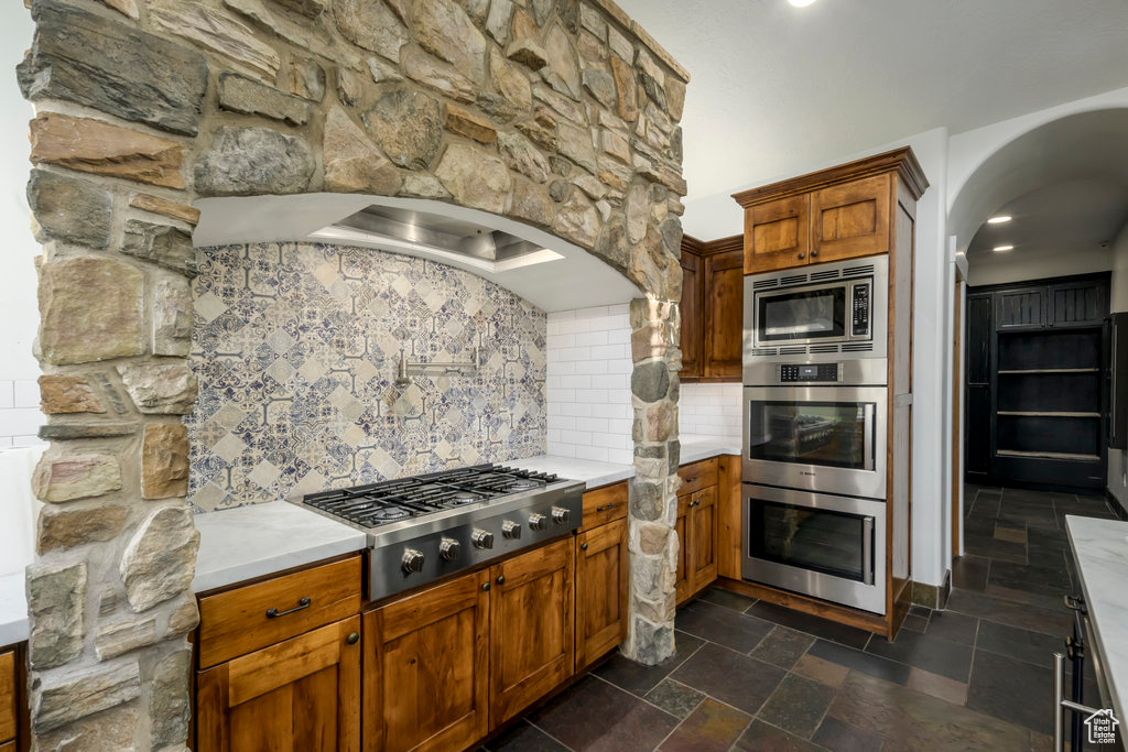 Kitchen with appliances with stainless steel finishes, dark tile flooring, and backsplash