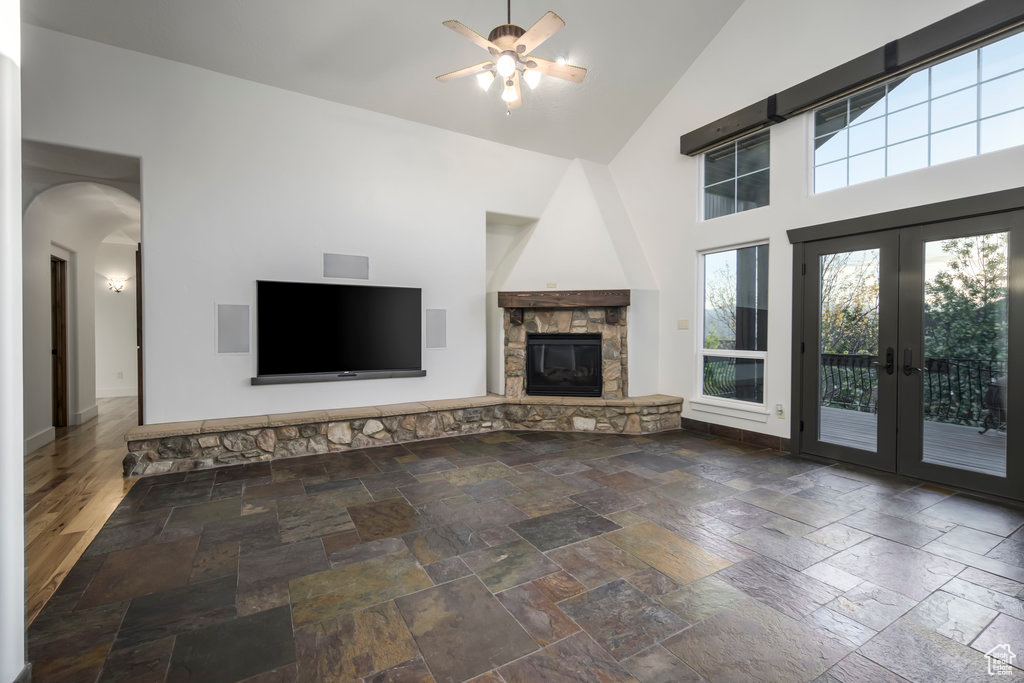 Unfurnished living room with ceiling fan, a stone fireplace, high vaulted ceiling, dark tile flooring, and french doors