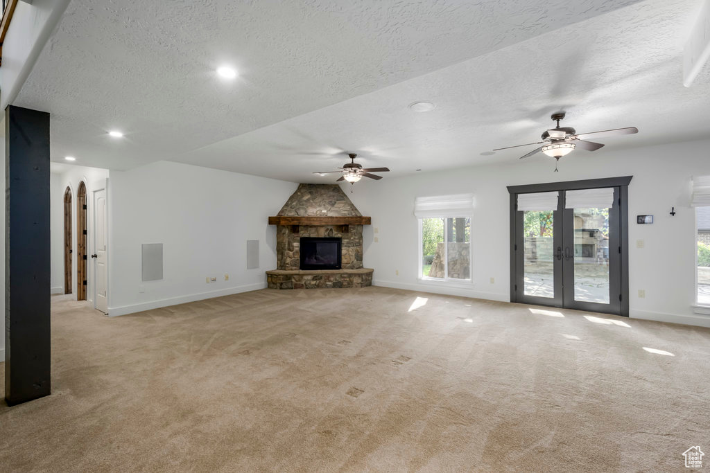 Unfurnished living room featuring light colored carpet, ceiling fan, and a stone fireplace