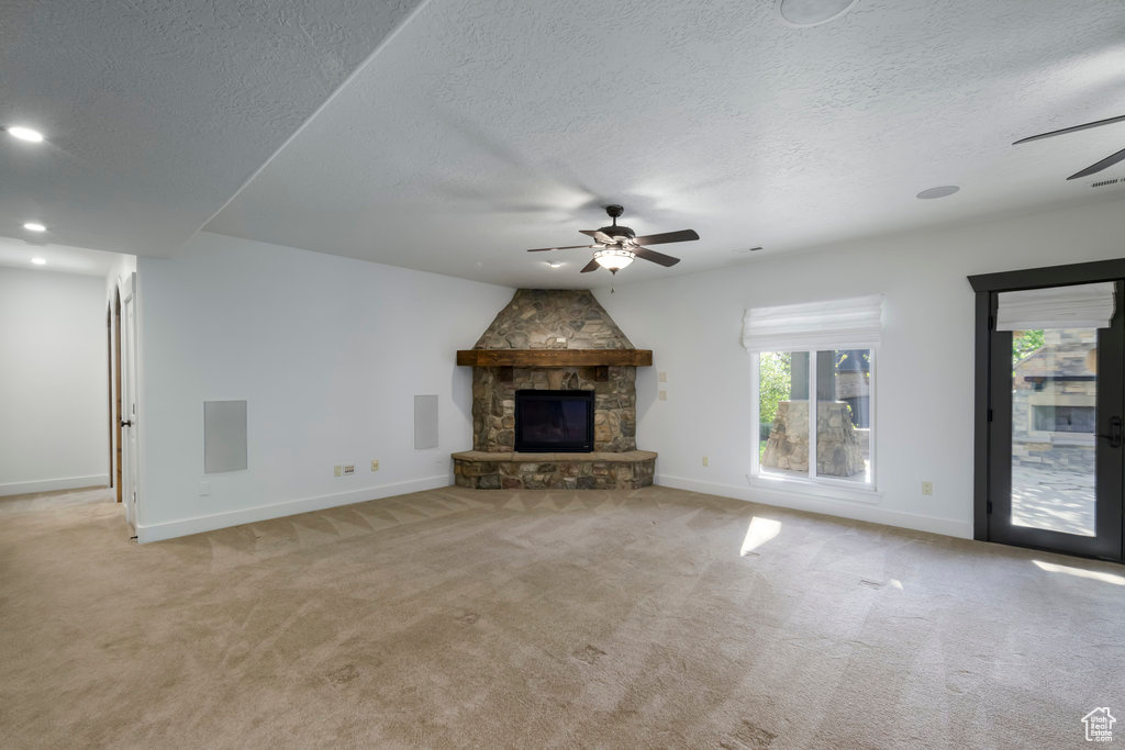 Unfurnished living room with light carpet, ceiling fan, a stone fireplace, and a textured ceiling