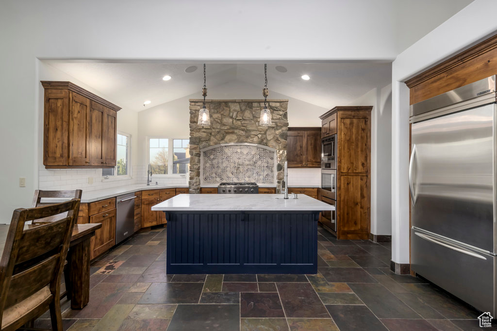 Kitchen featuring backsplash, lofted ceiling, stainless steel appliances, and a kitchen island with sink