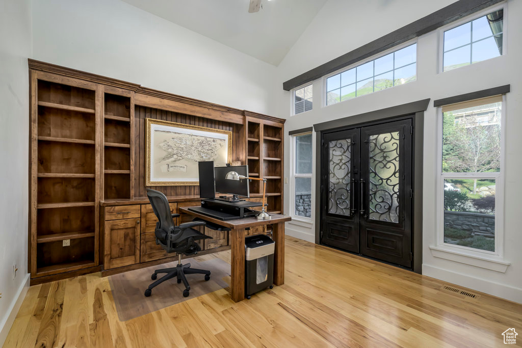 Home office with high vaulted ceiling, light hardwood / wood-style floors, and french doors