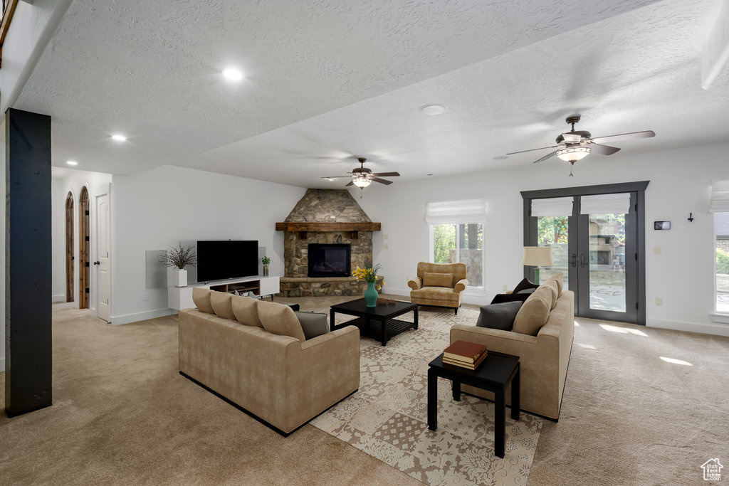 Carpeted living room featuring ceiling fan, a stone fireplace, and a textured ceiling