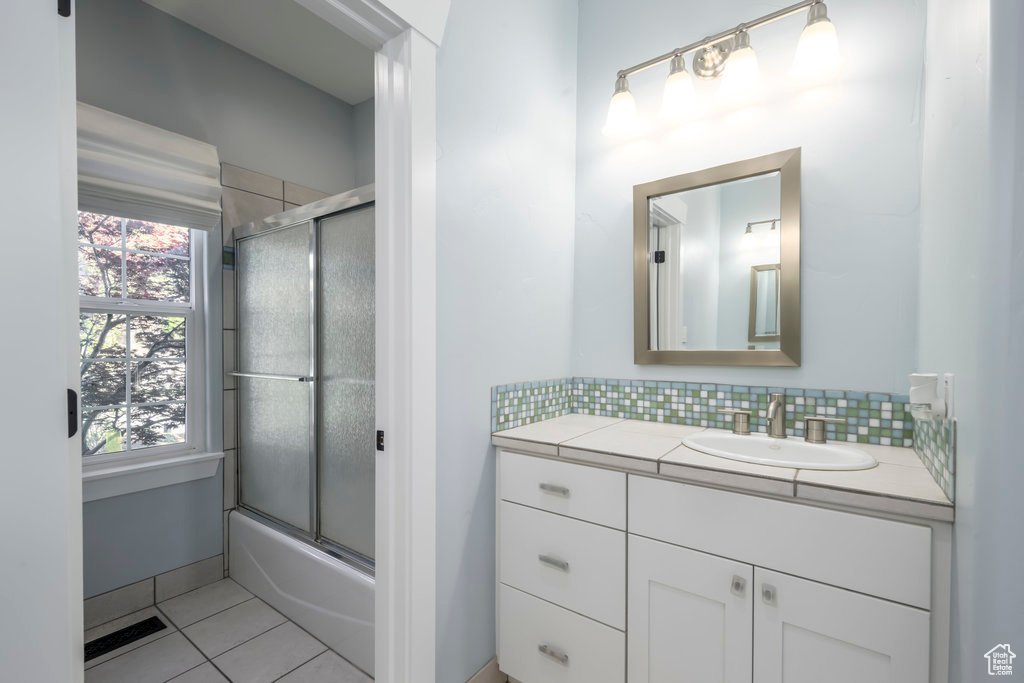 Bathroom with tasteful backsplash, vanity, tile floors, and enclosed tub / shower combo