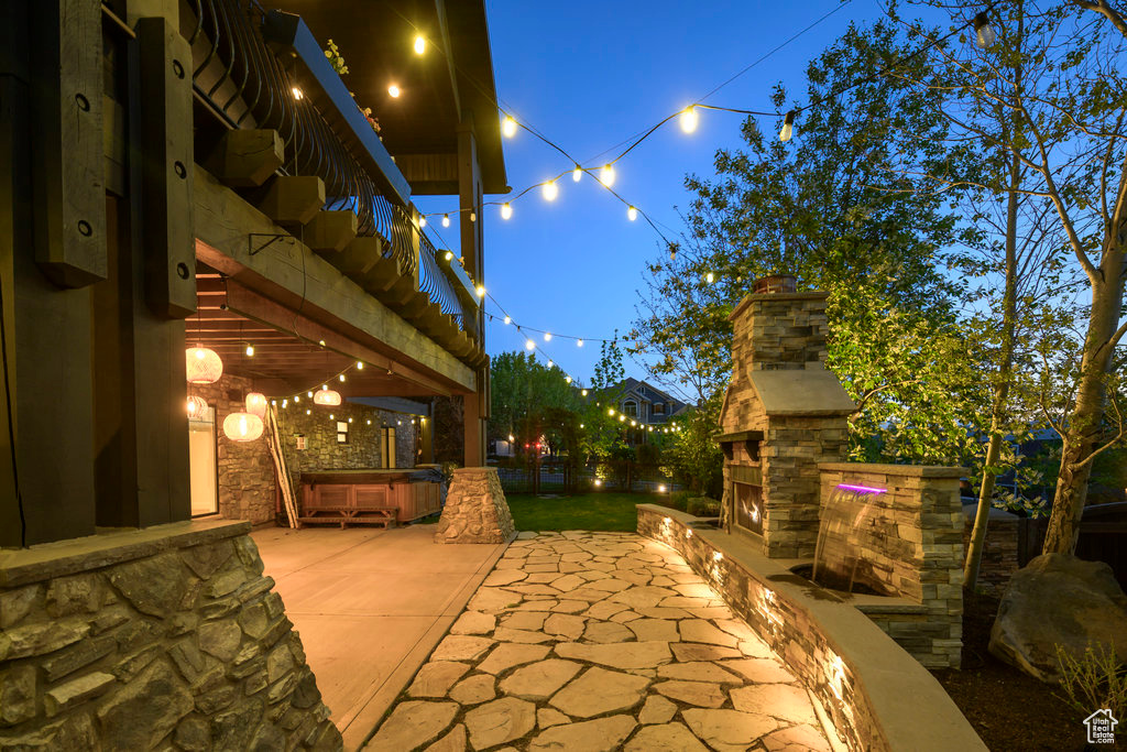 Patio terrace at twilight with an outdoor stone fireplace and a balcony