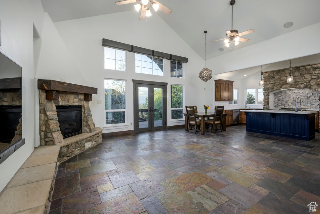 Unfurnished living room featuring tile flooring, high vaulted ceiling, ceiling fan, and a stone fireplace