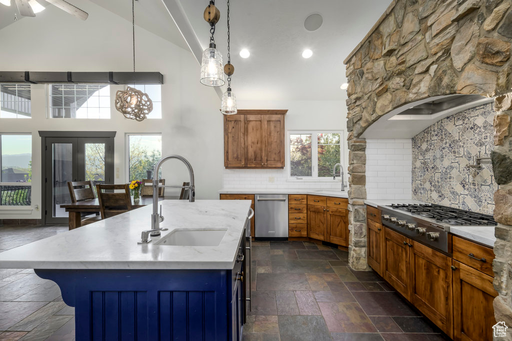 Kitchen with decorative light fixtures, sink, backsplash, and a kitchen island with sink