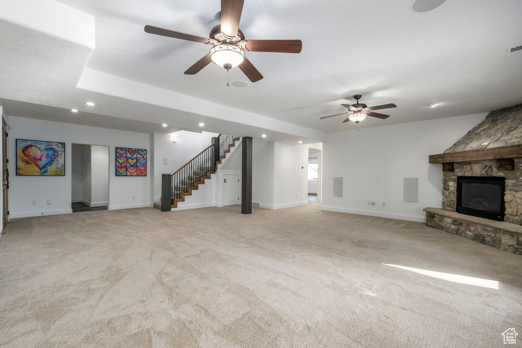 Unfurnished living room featuring light colored carpet, ceiling fan, a stone fireplace, and a textured ceiling