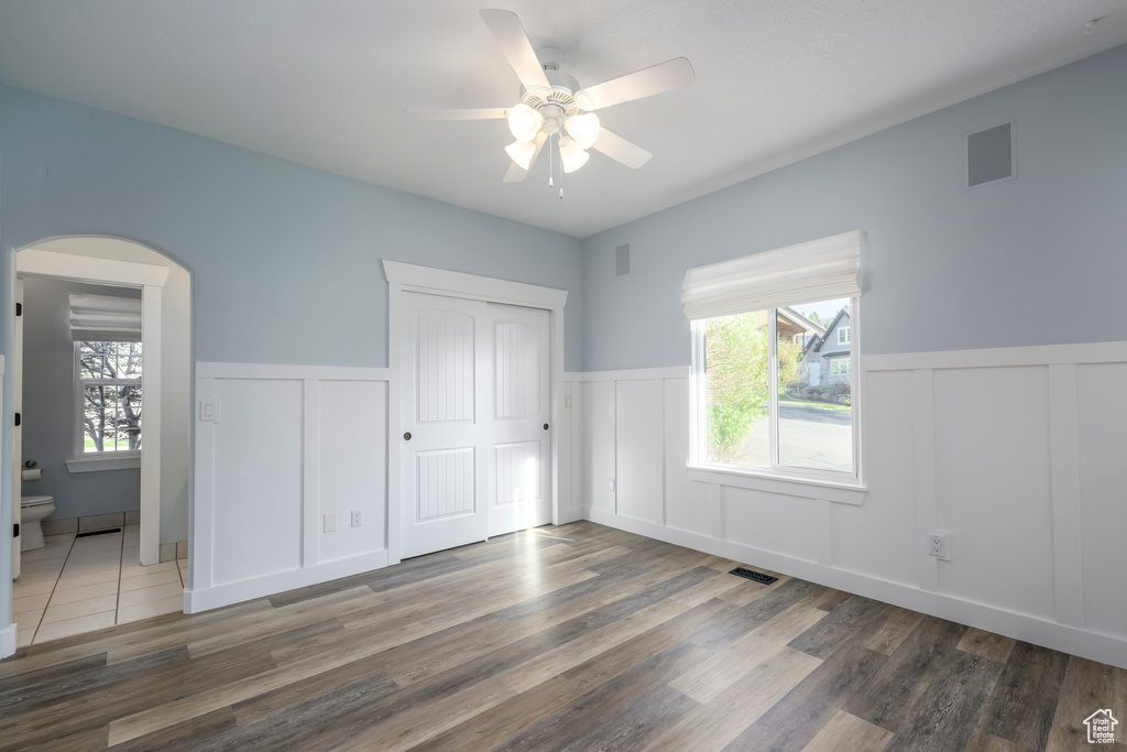 Unfurnished bedroom with ceiling fan, dark hardwood / wood-style flooring, ensuite bathroom, and multiple windows