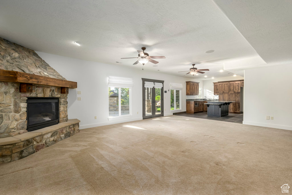 Unfurnished living room featuring a stone fireplace, carpet floors, ceiling fan, and a textured ceiling
